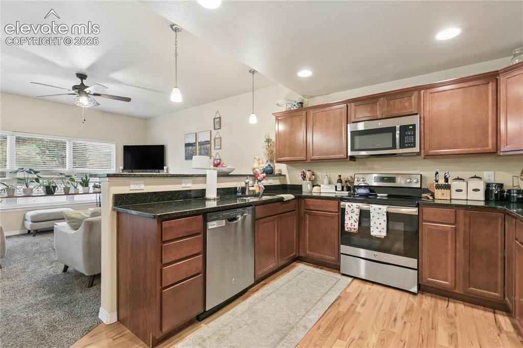 Image 2 of 28: U-shaped kitchen featuring wood-finish cabinetry, dark countertops, and sta