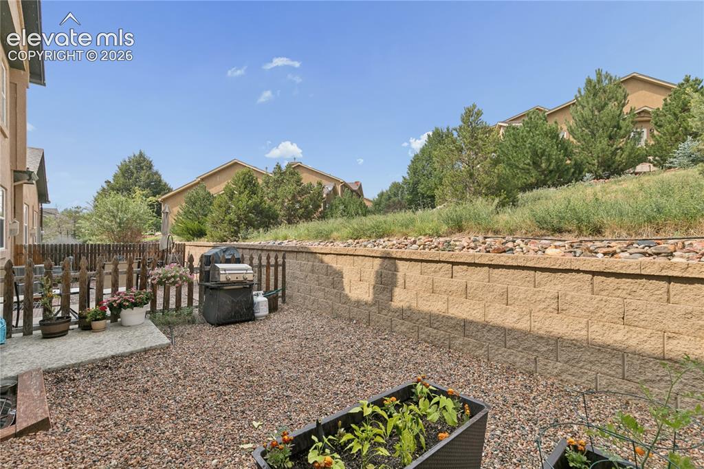 Image 20 of 28: Private backyard featuring a stone retaining wall, gravel ground cover, and