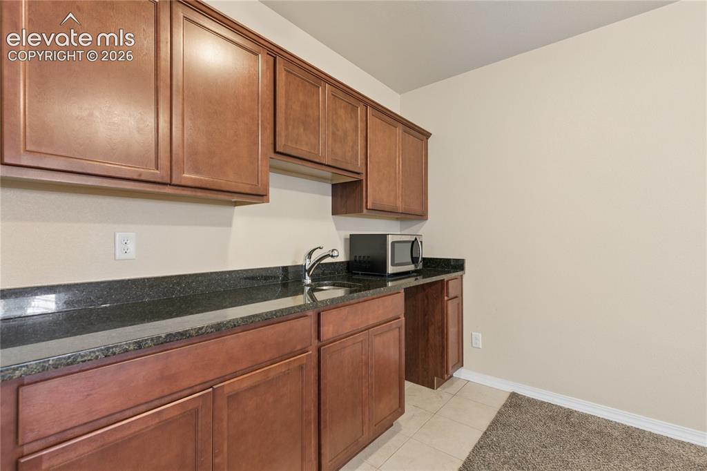 Image 24 of 28: Brown wood-finish cabinetry, dark stone countertops, undermount sink, and t