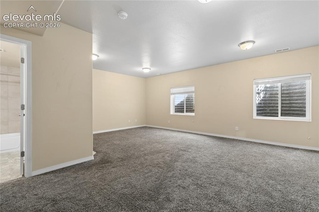 Image 25 of 28: Expansive room featuring plush gray carpeting, two windows with white blind