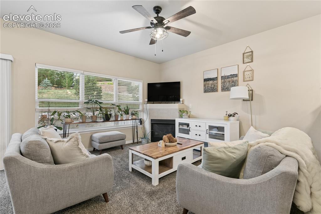 Image 5 of 28: Living area featuring a ceiling fan, fireplace with a mantle, and large win