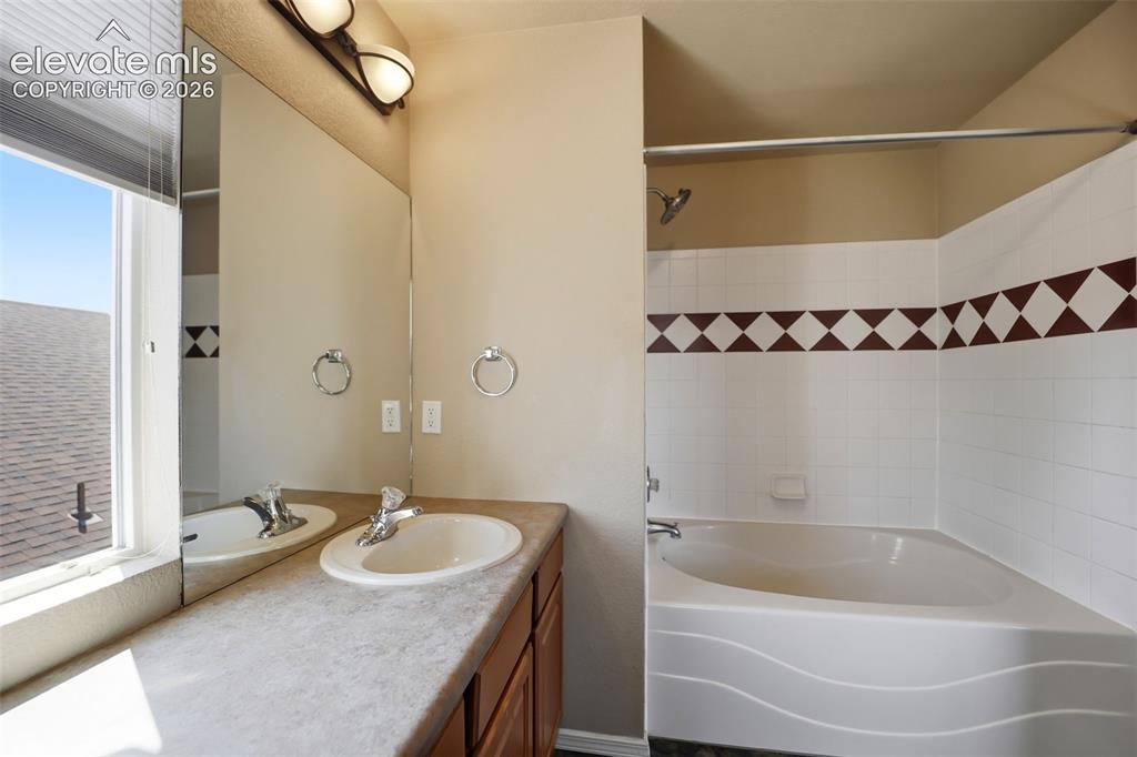 Image 25 of 47: Bathroom featuring a corner bathtub with white tile surround, a built-in va