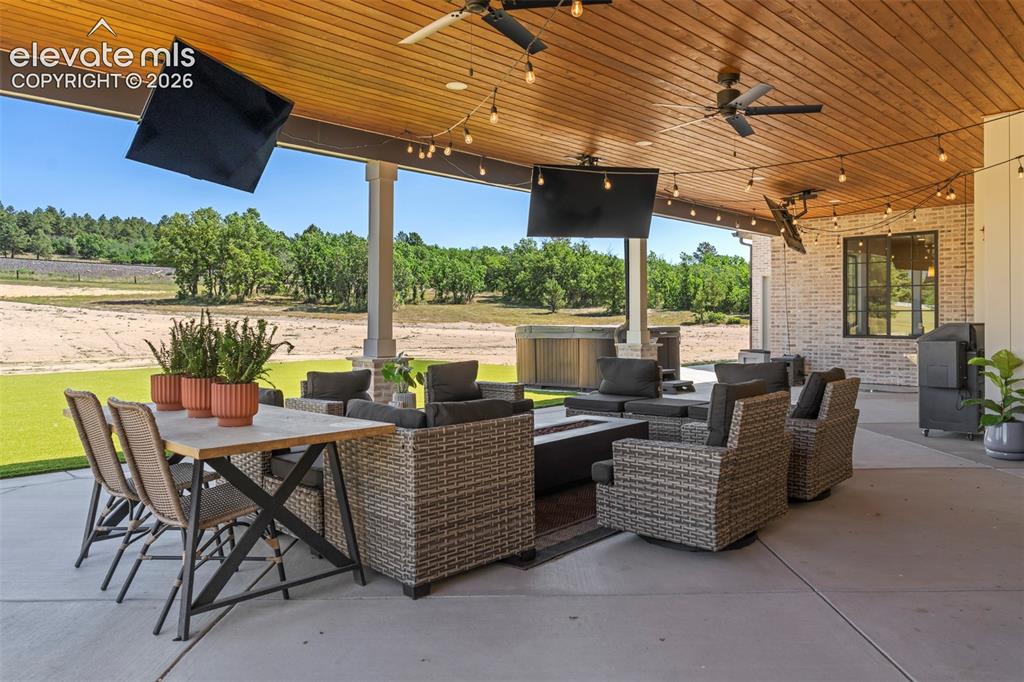 Image 46 of 49: Covered outdoor living area complete with seating, dining space, and TV for