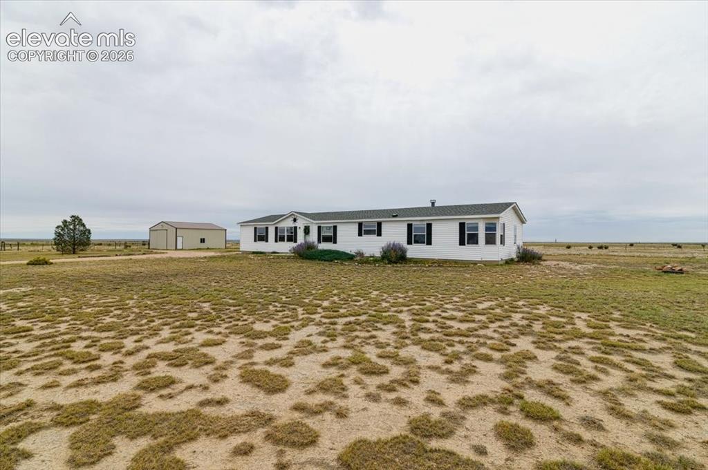 Image 18 of 23: White exterior residence with black shutters, green roof, and attached porc