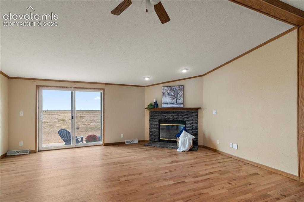 Image 6 of 23: Living area with wood-finish flooring, a stone-clad fireplace with a wood m