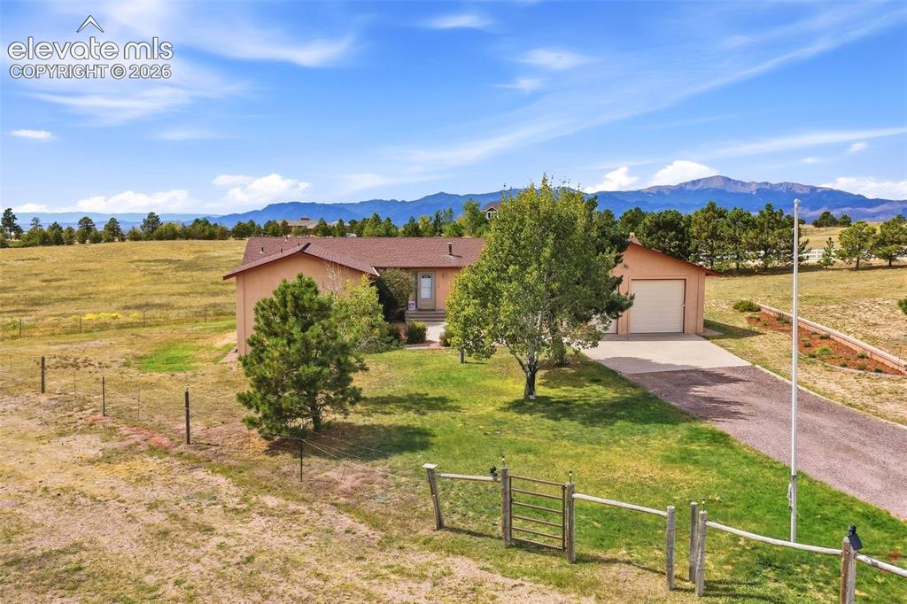 Caption: Ranch-style exterior with an attached oversized garage, paved driveway, and established trees
