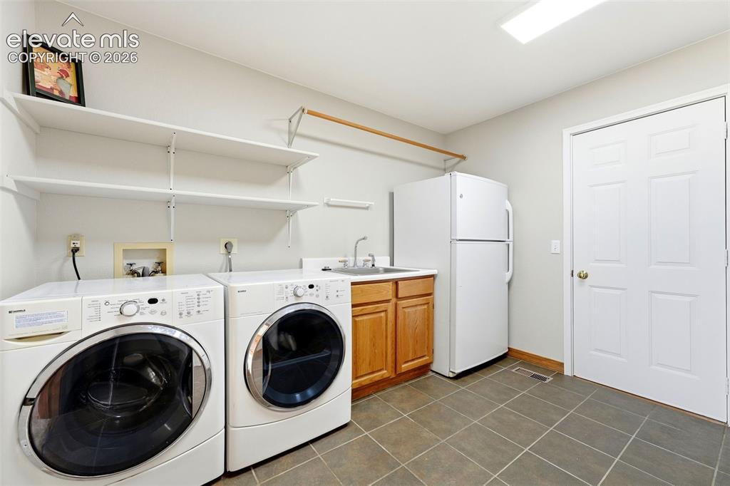 Image 17 of 50: Tile flooring, built-in shelving, wood-finish cabinetry, utility sink, and 