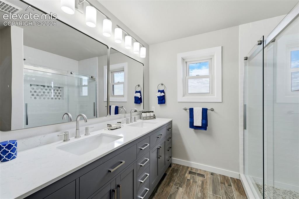 Image 21 of 50: Dual-sink vanity with a light countertop, wood-finish flooring, and a glass