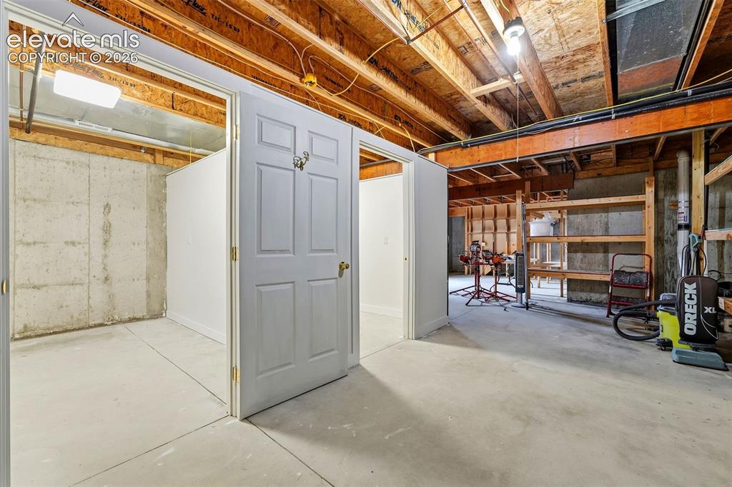 Image 31 of 50: Unfinished lower level with concrete flooring, exposed wood beam ceiling, a