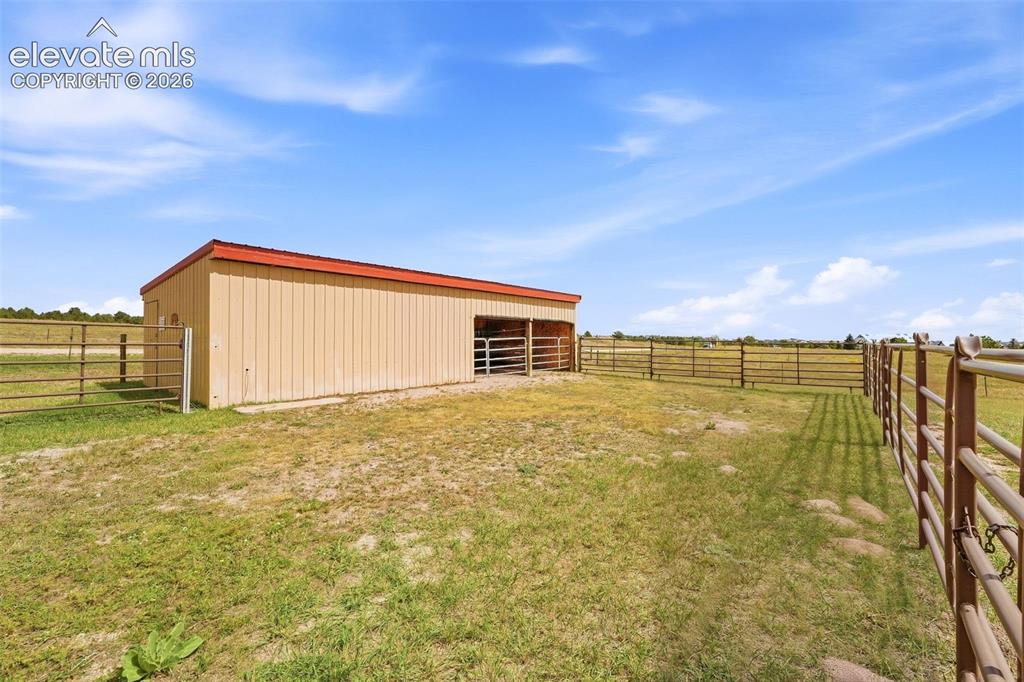 Image 36 of 50: Metal-sided outbuilding with a red roof, multiple fenced enclosures, and a 