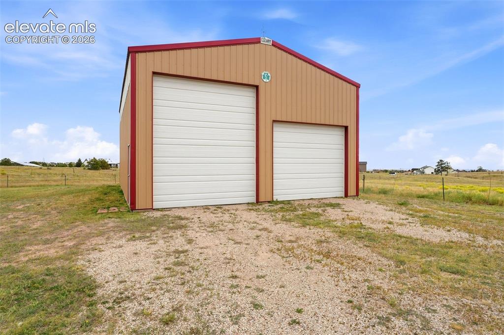 Image 40 of 50: Metal building with a gambrel roof and two white roll-up doors