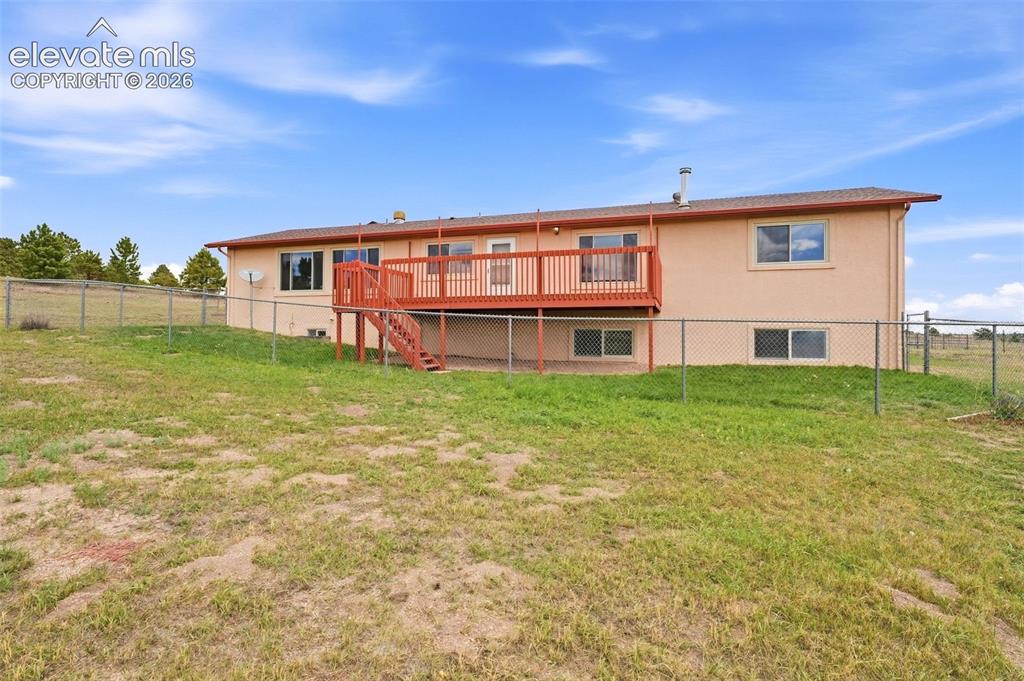 Image 43 of 50: Expansive sloped yard featuring chain link fencing and a stucco exterior wi