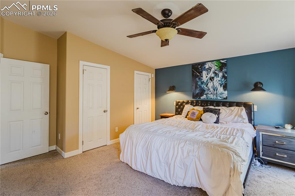 Image 10 of 30: Bedroom featuring light carpet, two closets, a ceiling fan, and vaulted cei