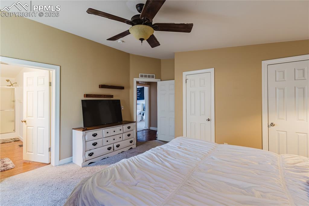 Image 12 of 30: Bedroom with carpet floors, a ceiling fan, multiple closets, and ensuite ba
