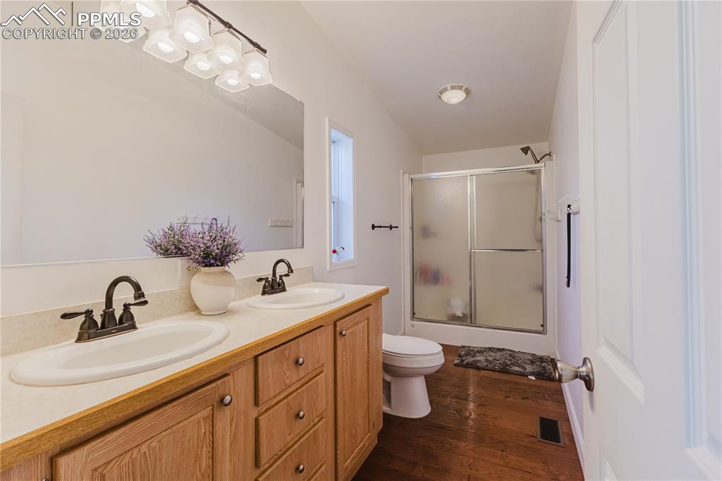 Image 13 of 30: Bathroom with a shower stall, double vanity, and dark wood finished floors