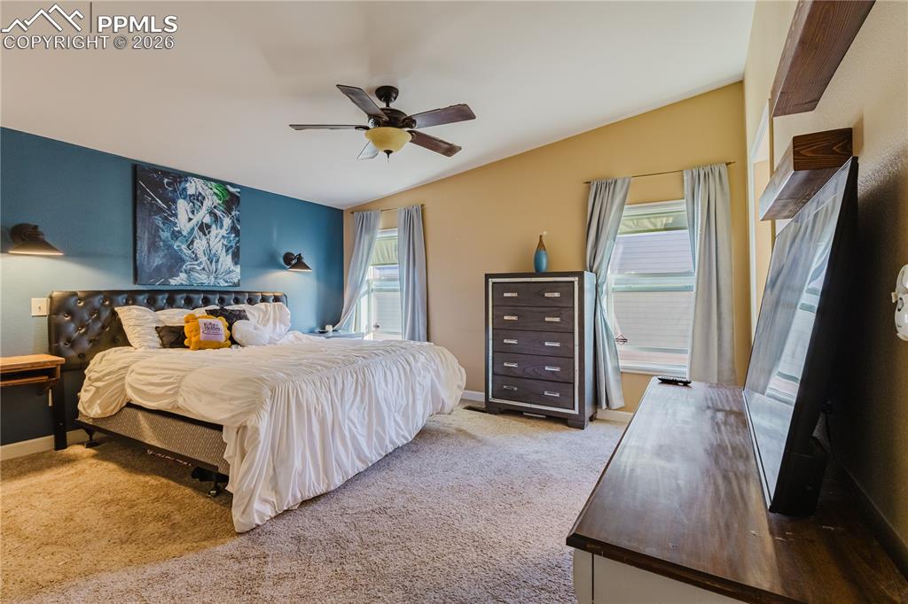 Image 19 of 30: Bedroom featuring light carpet, vaulted ceiling, multiple windows, and ceil