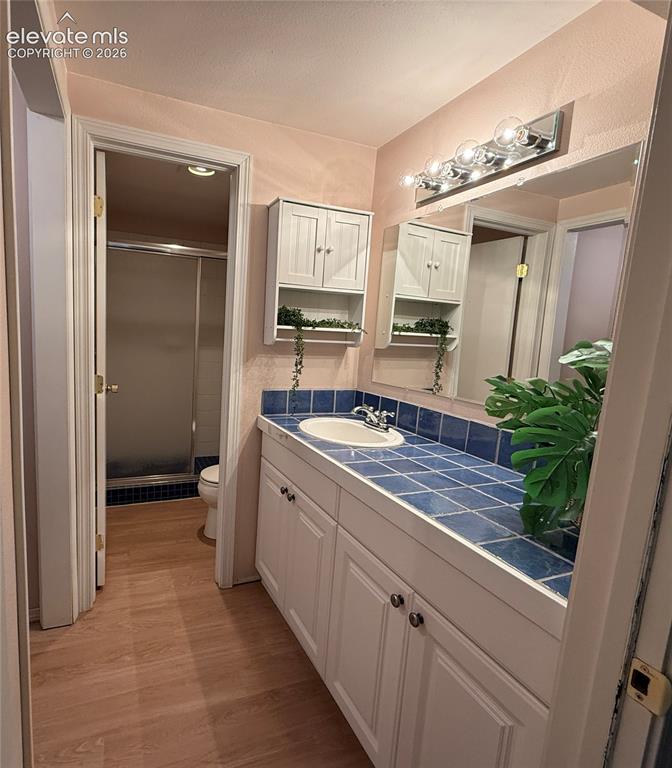 Image 19 of 26: Vanity featuring a tiled countertop, sink, white shaker-style cabinetry, wa