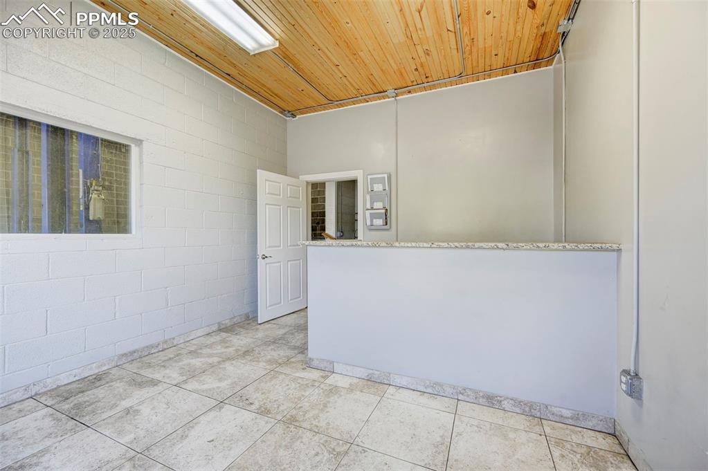 Image 22 of 42: Empty room with wood ceiling, concrete block wall, and light tile patterned