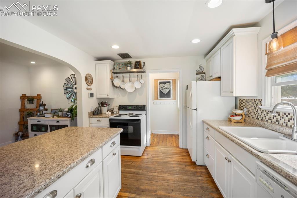 Image 11 of 47: Kitchen with white appliances, arched walkways, white cabinets, wood finish
