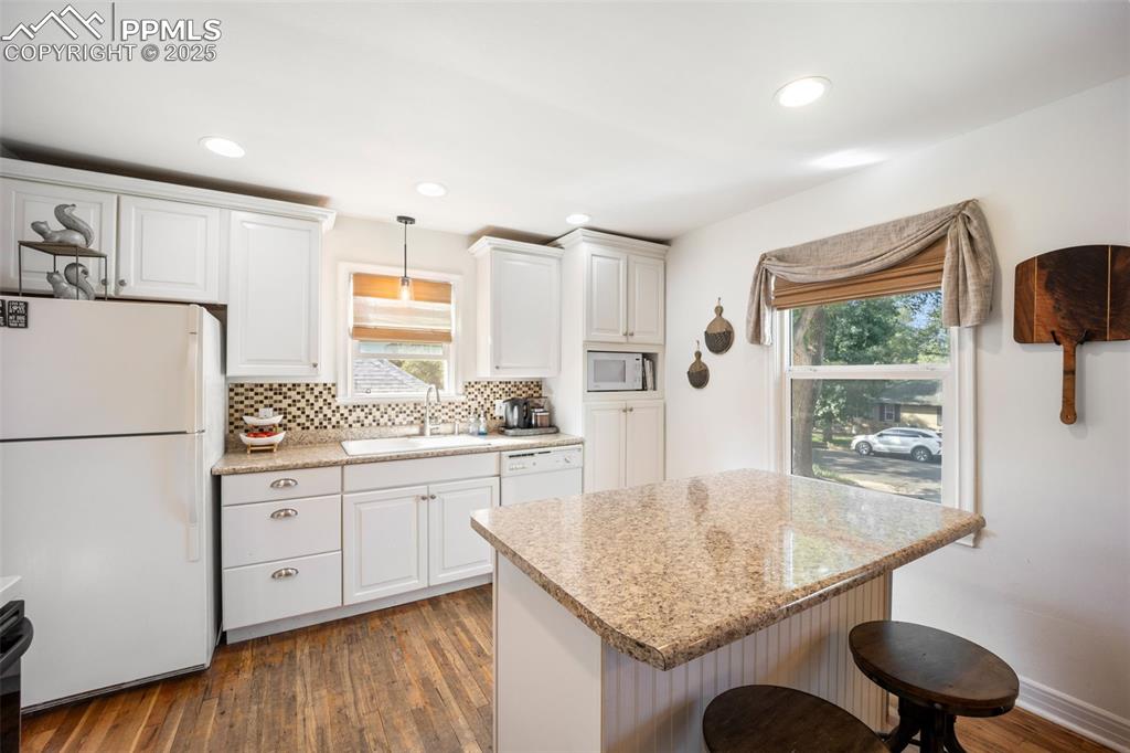 Image 9 of 47: Kitchen with white appliances, a breakfast bar, decorative backsplash, wood