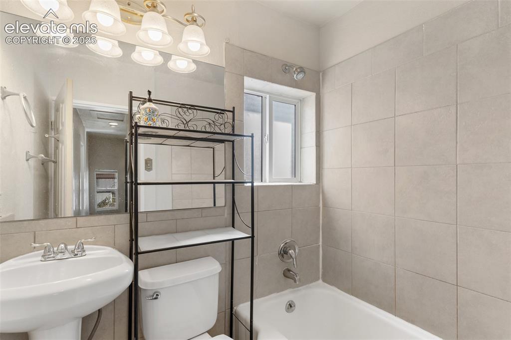 Image 38 of 42: Pedestal sink, full-width wall mirror, ceramic wall tiling, shower-tub comb