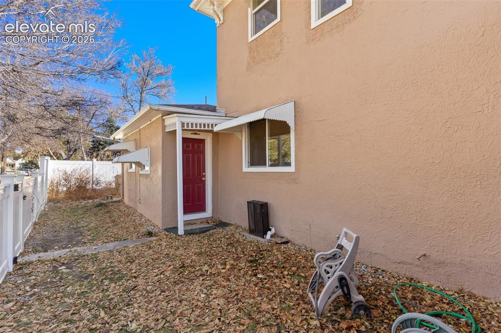 Image 42 of 42: Stucco exterior with multiple windows, a red entry door, and a white fence
