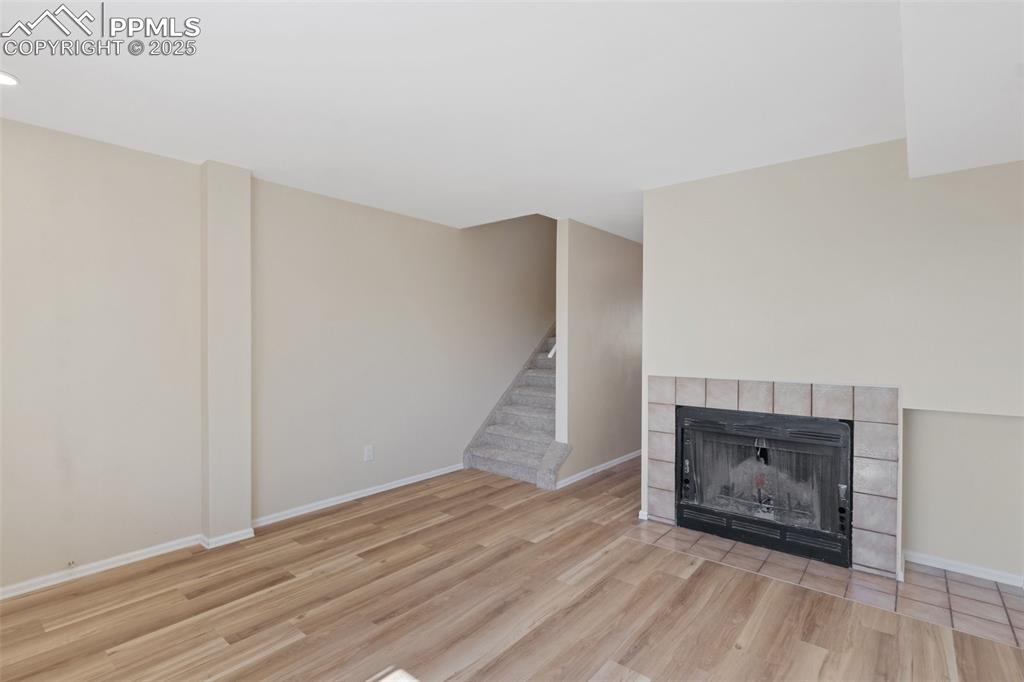 Image 4 of 26: Unfurnished living room with a fireplace, wood finished floors, and stairwa