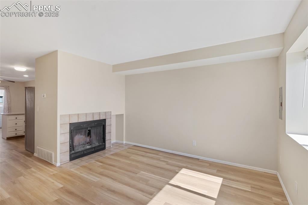 Image 5 of 26: Unfurnished living room featuring a tiled fireplace and light wood-type flo