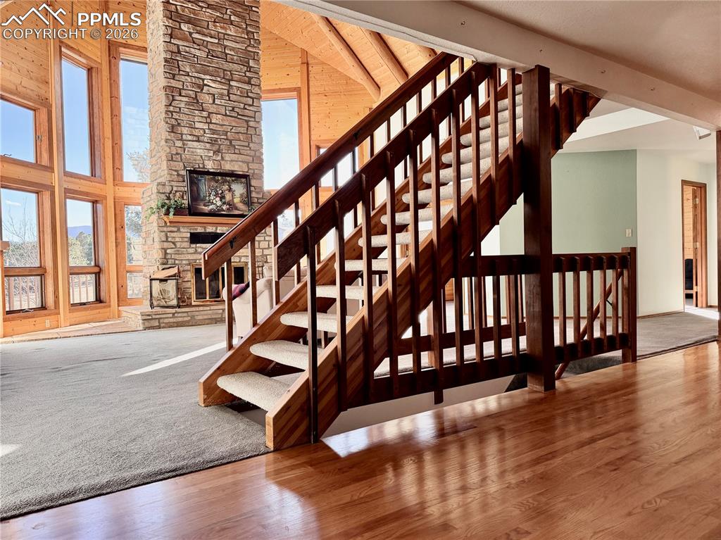 Image 12 of 45: Stairway featuring a high ceiling, wood finished floors, and a stone firepl