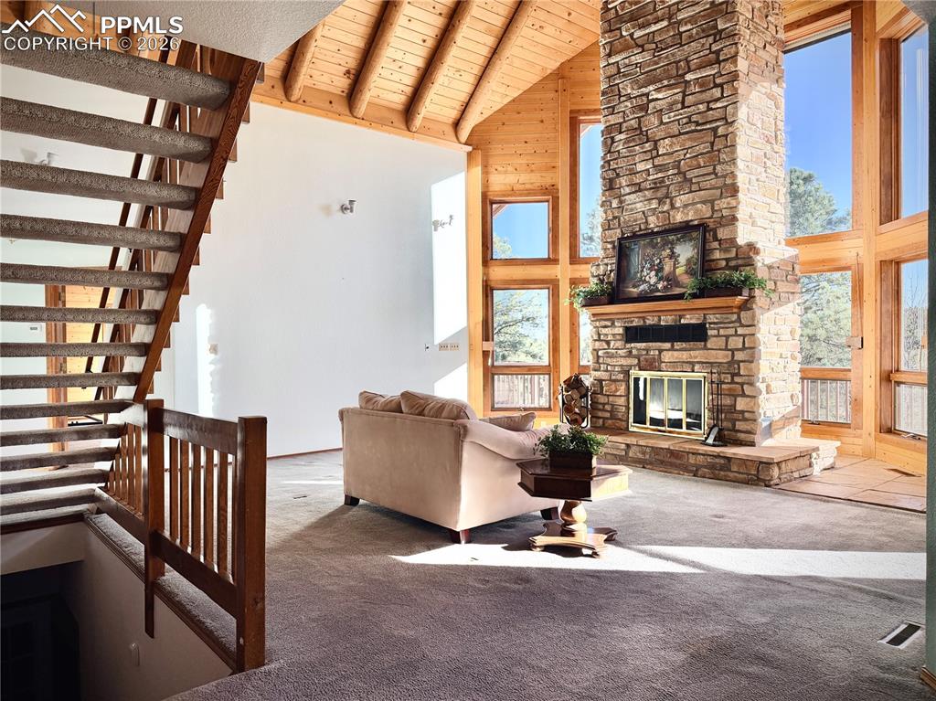 Image 13 of 45: Living area with a high wooden beamed ceiling, carpet floors, a stone firep