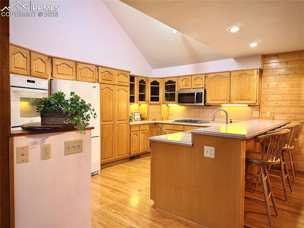 Image 18 of 45: Kitchen with lofted ceiling, white appliances, glass insert cabinets, light