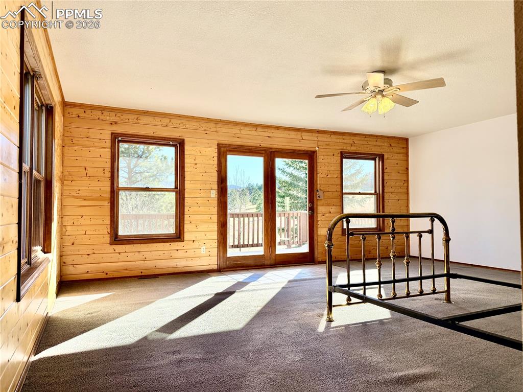 Image 22 of 45: Bedroom with carpet, wood walls, access to outside, ceiling fan, and a text