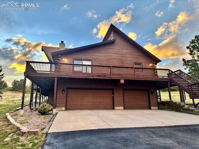 Image 7 of 45: View of front facade with a deck, driveway, a chimney, and an attached gara