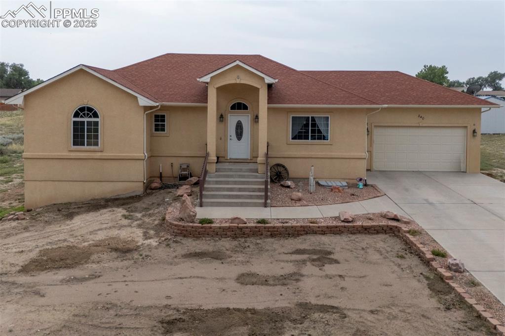 Caption: View of front of property with a shingled roof, stucco siding, concrete driveway, and a garage
