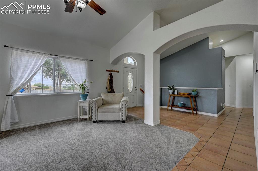 Image 11 of 47: Living area with light tile patterned floors, lofted ceiling, ceiling fan, 