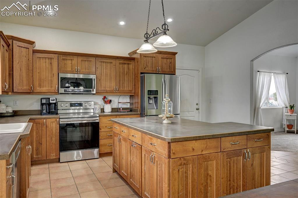 Image 14 of 47: Kitchen with brown cabinetry, appliances with stainless steel finishes, han