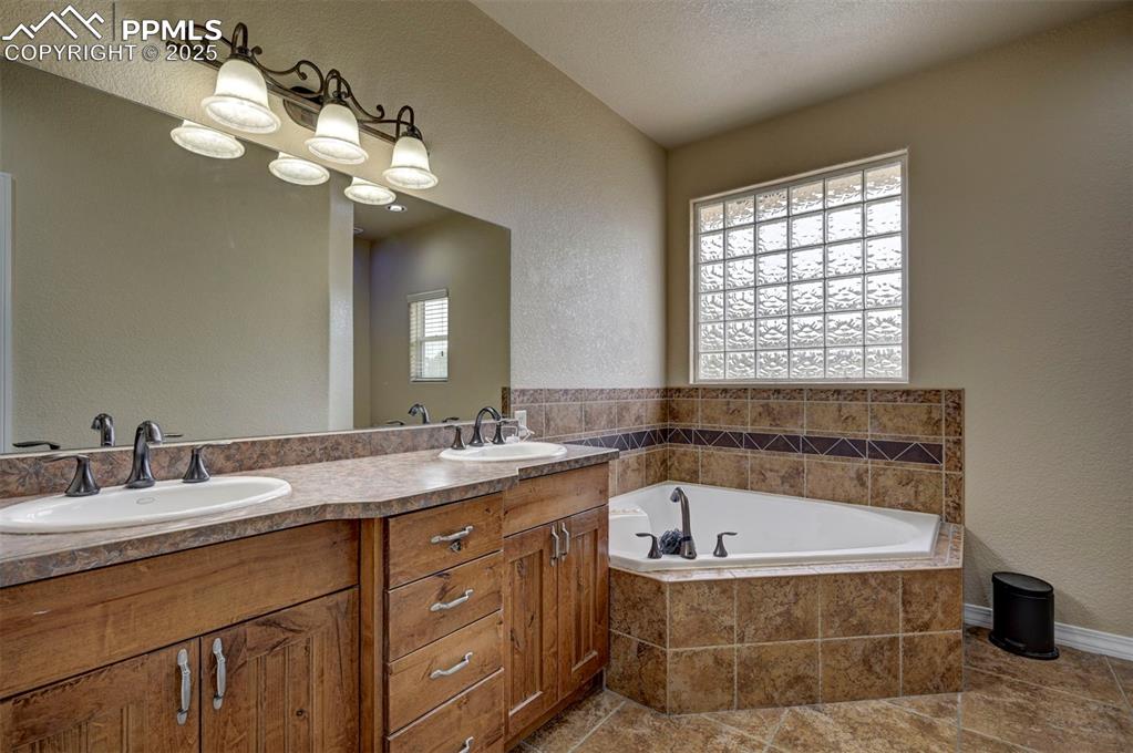 Image 24 of 47: Bathroom with a textured wall, a garden tub, double vanity, and tile patter