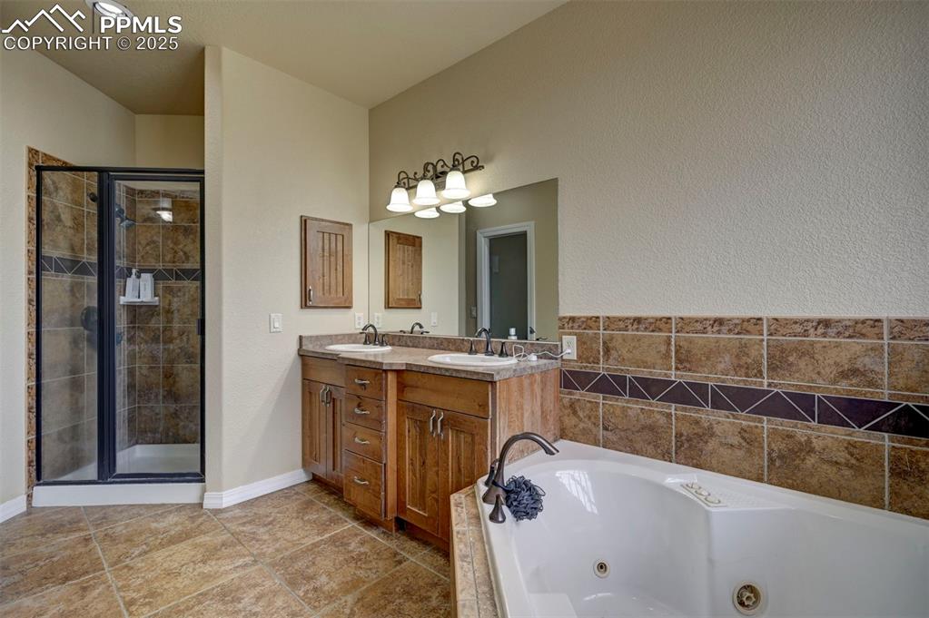 Image 25 of 47: Full bath featuring double vanity, a whirlpool tub, a shower stall, light t