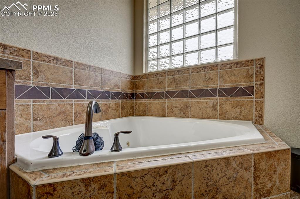 Image 26 of 47: Full bathroom with a textured wall, a whirlpool tub, and plenty of natural 