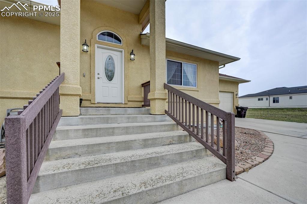 Image 3 of 47: Doorway to property with stucco siding, a garage, and concrete driveway