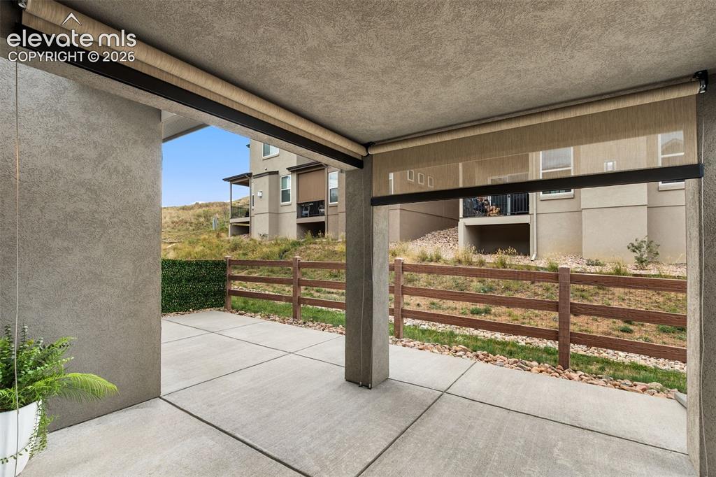 Image 11 of 43: Covered patio with concrete flooring, stucco walls, and roll-down sun shade