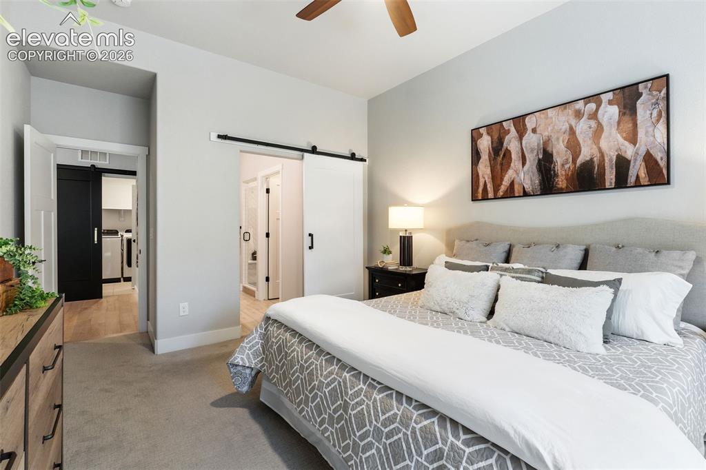 Image 26 of 43: Carpeted room featuring a ceiling fan, a headboard, and a wall-mounted ligh