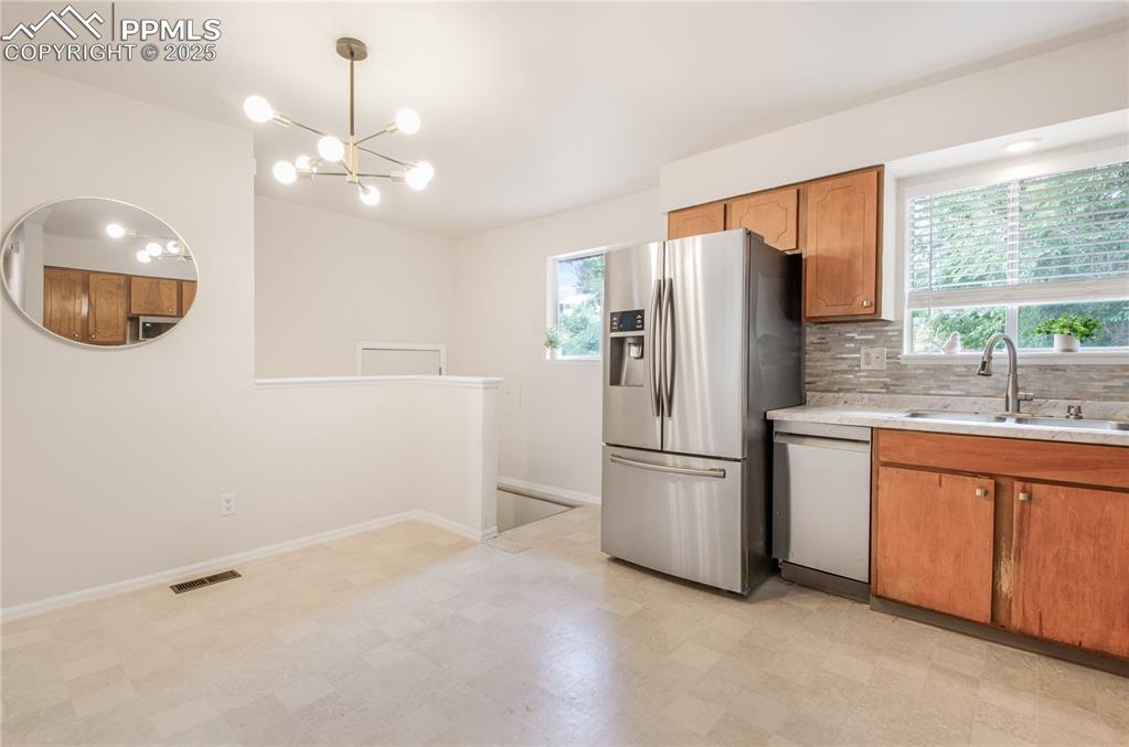 Image 6 of 25: Kitchen with stainless steel fridge, white dishwasher, light countertops, b