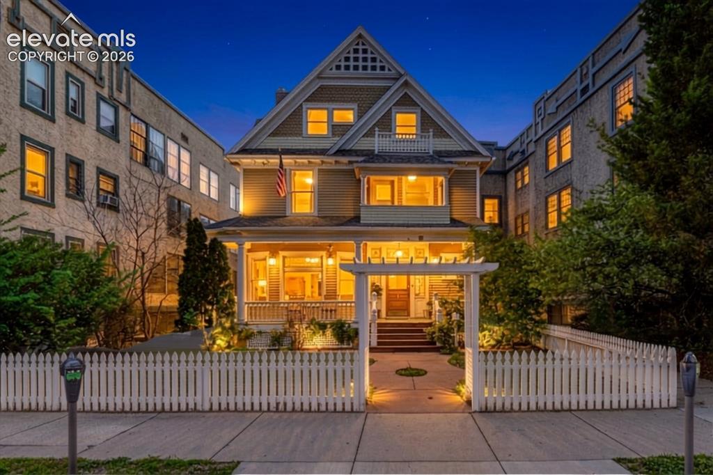 Caption: Victorian-style residence featuring a welcoming front porch, white picket fence, and a decorative ar