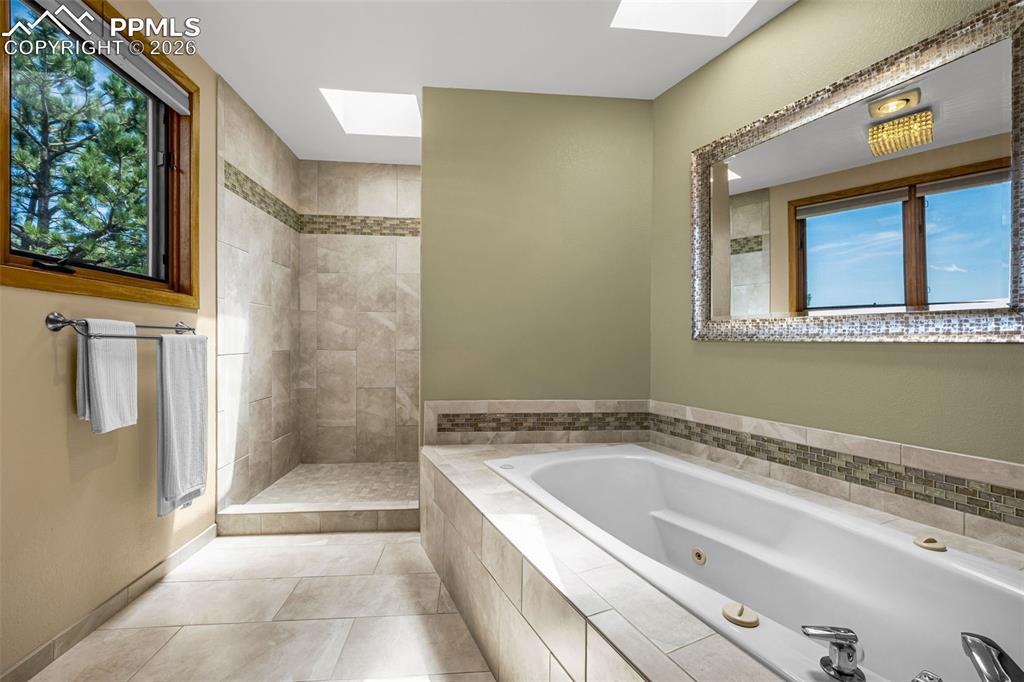 Image 15 of 42: Full bath with a skylight, tiled shower, a jetted tub, and light tile patte