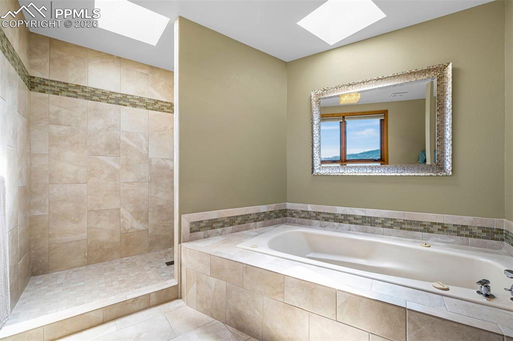 Image 16 of 42: Bathroom featuring a skylight, tiled shower, light tile patterned floors, a