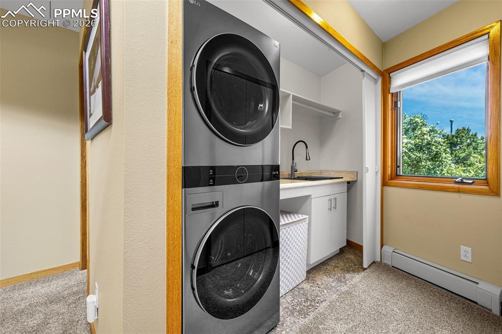 Image 19 of 42: Laundry area with a baseboard heating unit, light carpet, and stacked washe