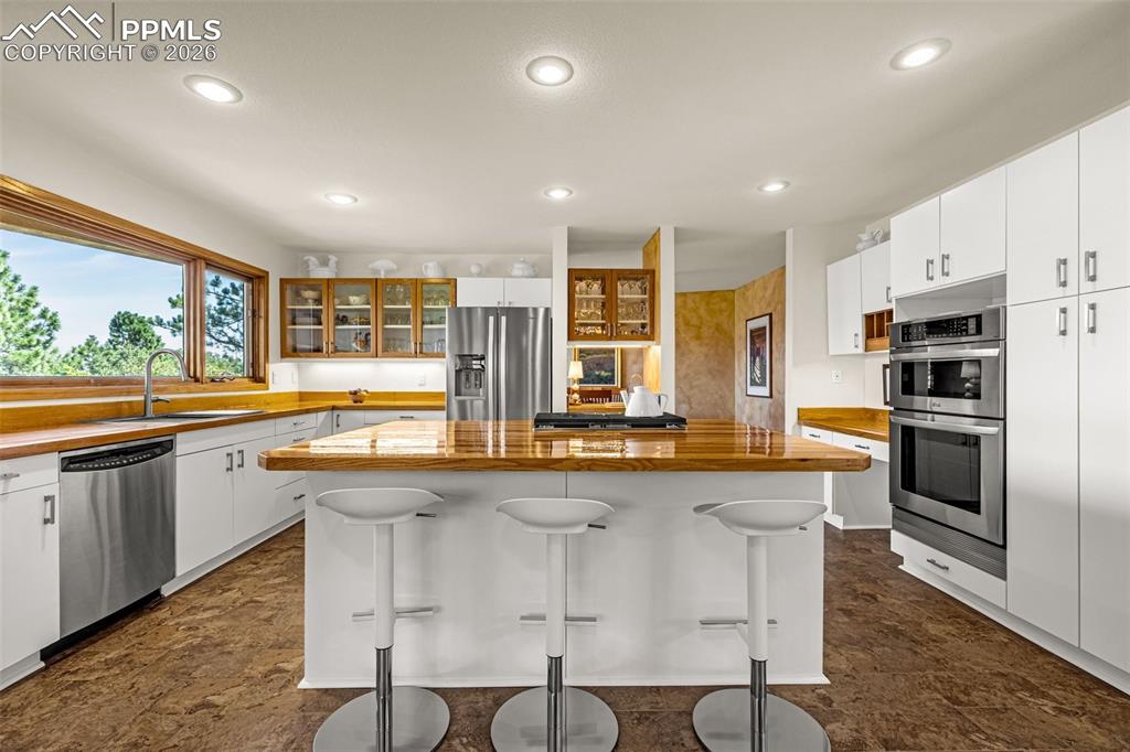 Image 5 of 42: Kitchen with wooden counters, glass insert cabinets, white cabinetry, stain