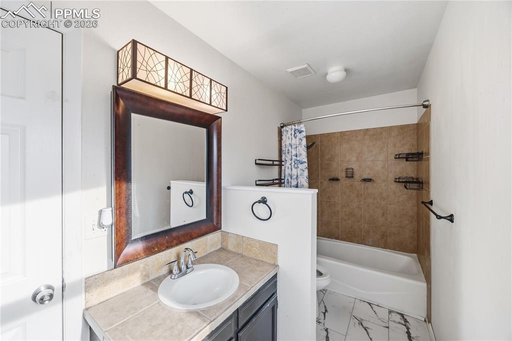 Image 16 of 27: The primary bathroom features a vanity, framed mirror, and tiled tub/shower