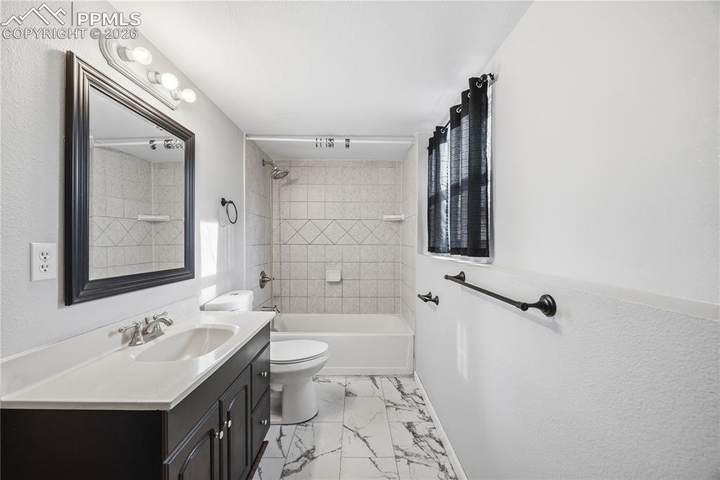 Image 21 of 27: Lower level full batrhoom with vanity, framed mirror, and tiled tub/shower.
